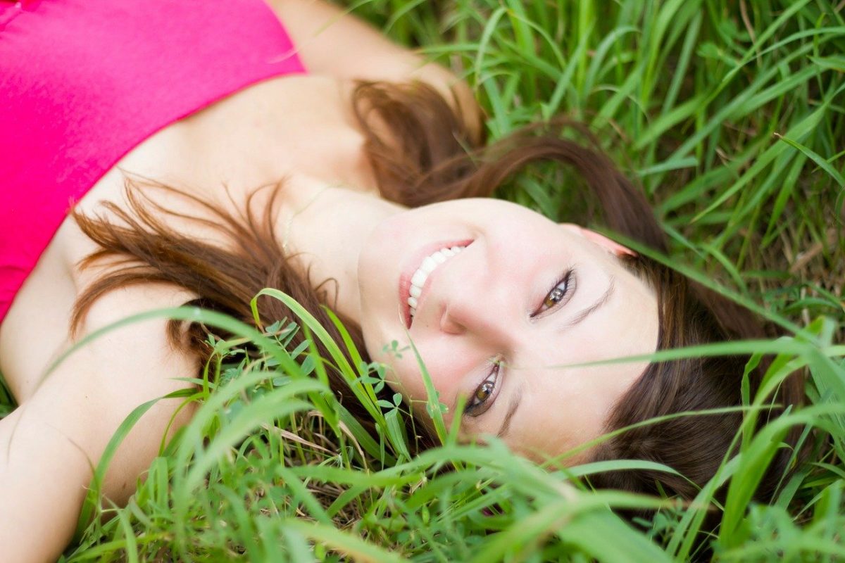 Jeune femme souriante, allongée sur des herbes hautes.