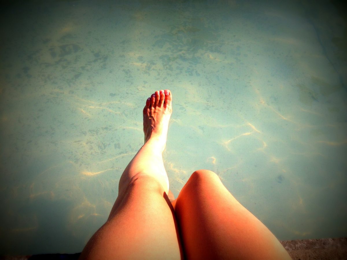 Au dessus de l'eau, jambes d'une jeune femme assise au bord d'un bassin