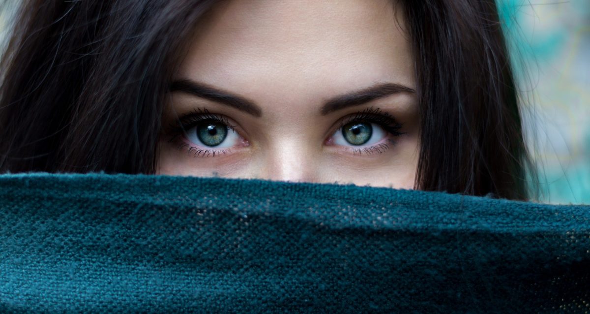 viasge en gros plan d'une jeune femme aux beaux yeux bleus et dont le bas du visage est dissimulé par une étoffe laineuse bleu pétrôle.